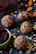 Round energy balls with bits of oats and dried fruit are displayed on a dark surface. A small bowl filled with dried cranberries is nearby, surrounded by scattered oats and almonds.