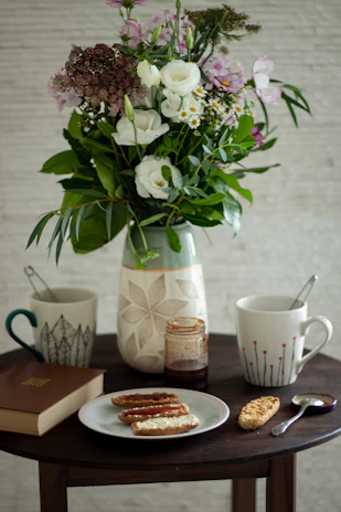 A table set for a slow morning with a mix of vibrant plates, mugs, and a small vase holding fresh wildflowers.