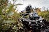 An ATV powering through a muddy forest trail, splashing water and mud around.