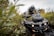An ATV splashing through a muddy puddle surrounded by dense foliage.