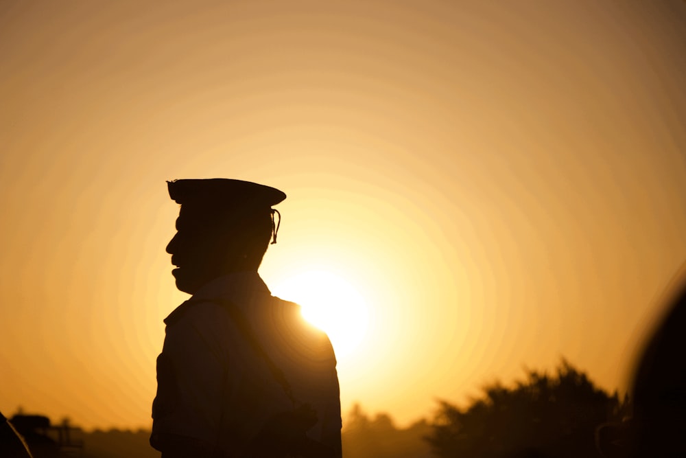 a silhouette of a man wearing a hat at sunset