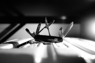 A multi-tool pocket knife is centrally displayed with its various components unfolded, including scissors, a screwdriver, and a bottle opener. The lighting casts dramatic shadows, emphasizing the sleek design of the knife against a blurred background.