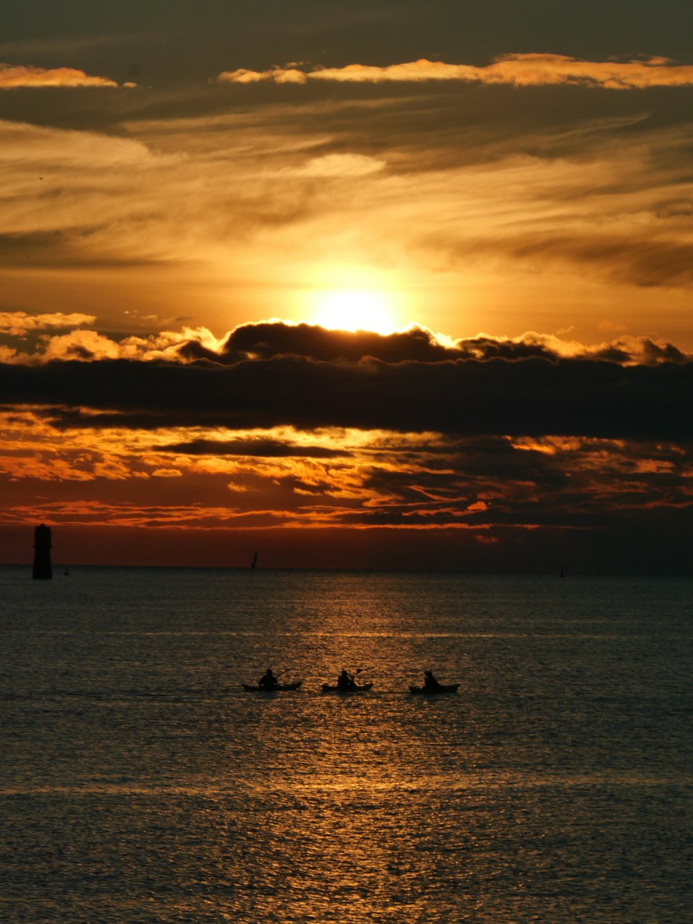 the sun is setting over the ocean with three boats in the water