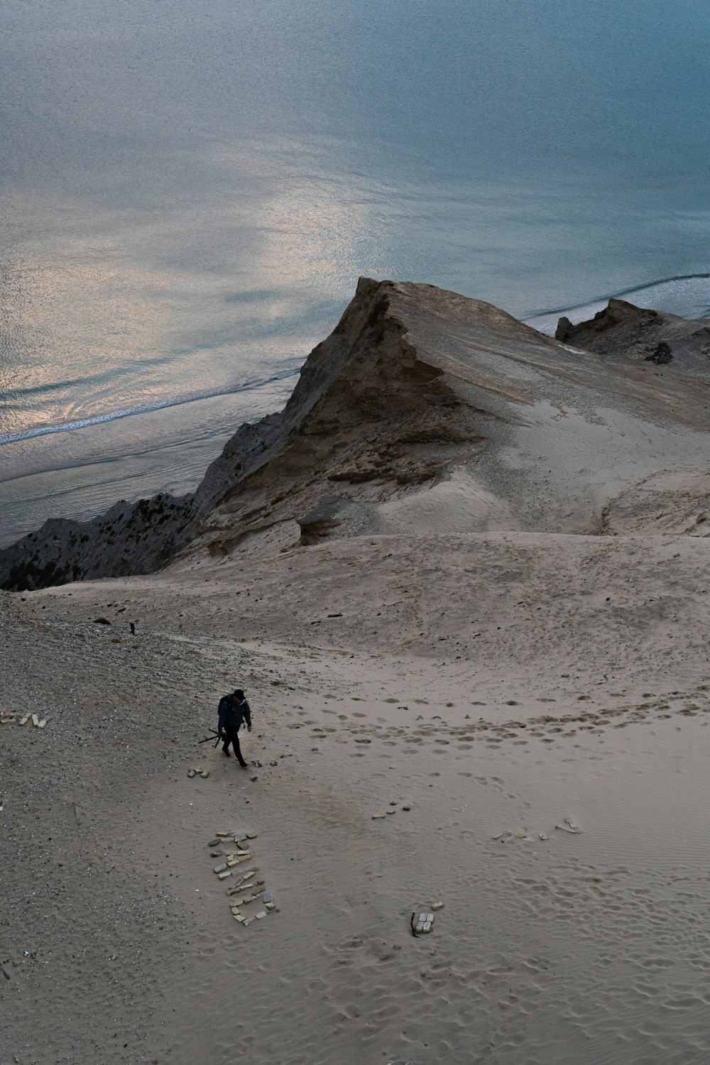 a man walking across a sandy beach next to the ocean