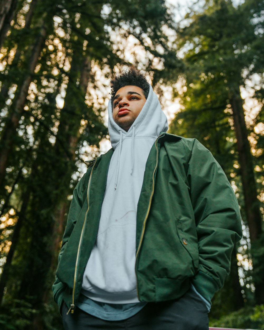 a man in a green jacket standing in front of trees