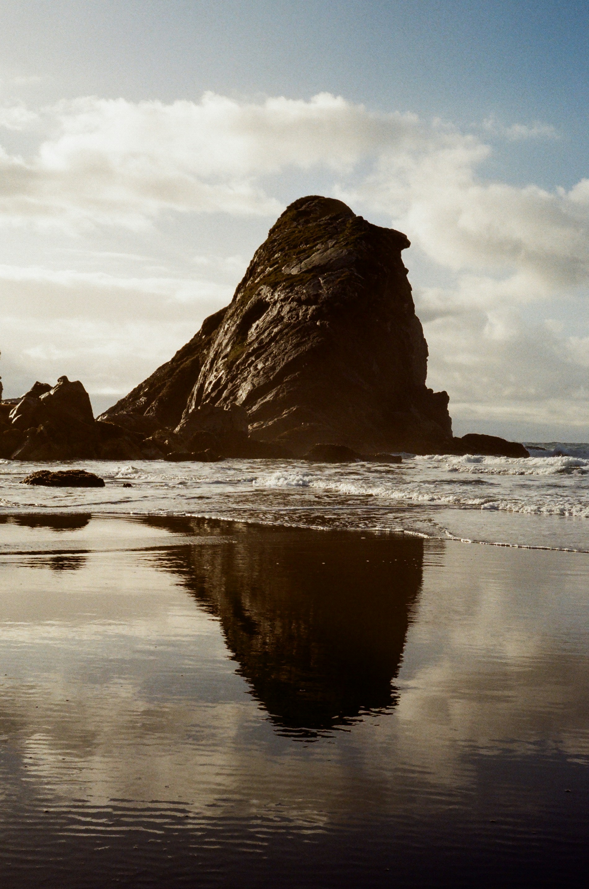 a large rock sitting on top of a beach next to the ocean
