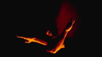An artistic shot of a silhouette of a person in a provocative pose against a warm background.