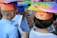 Children wearing colorful paper hats with educational-themed designs are viewing illustrated books. The hats are decorated with images of books and cartoon faces, suggesting a celebration or educational event.