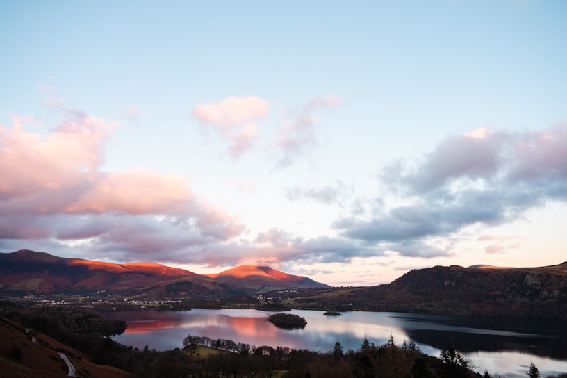 A serene landscape featuring a calm lake surrounded by mountains at sunrise.