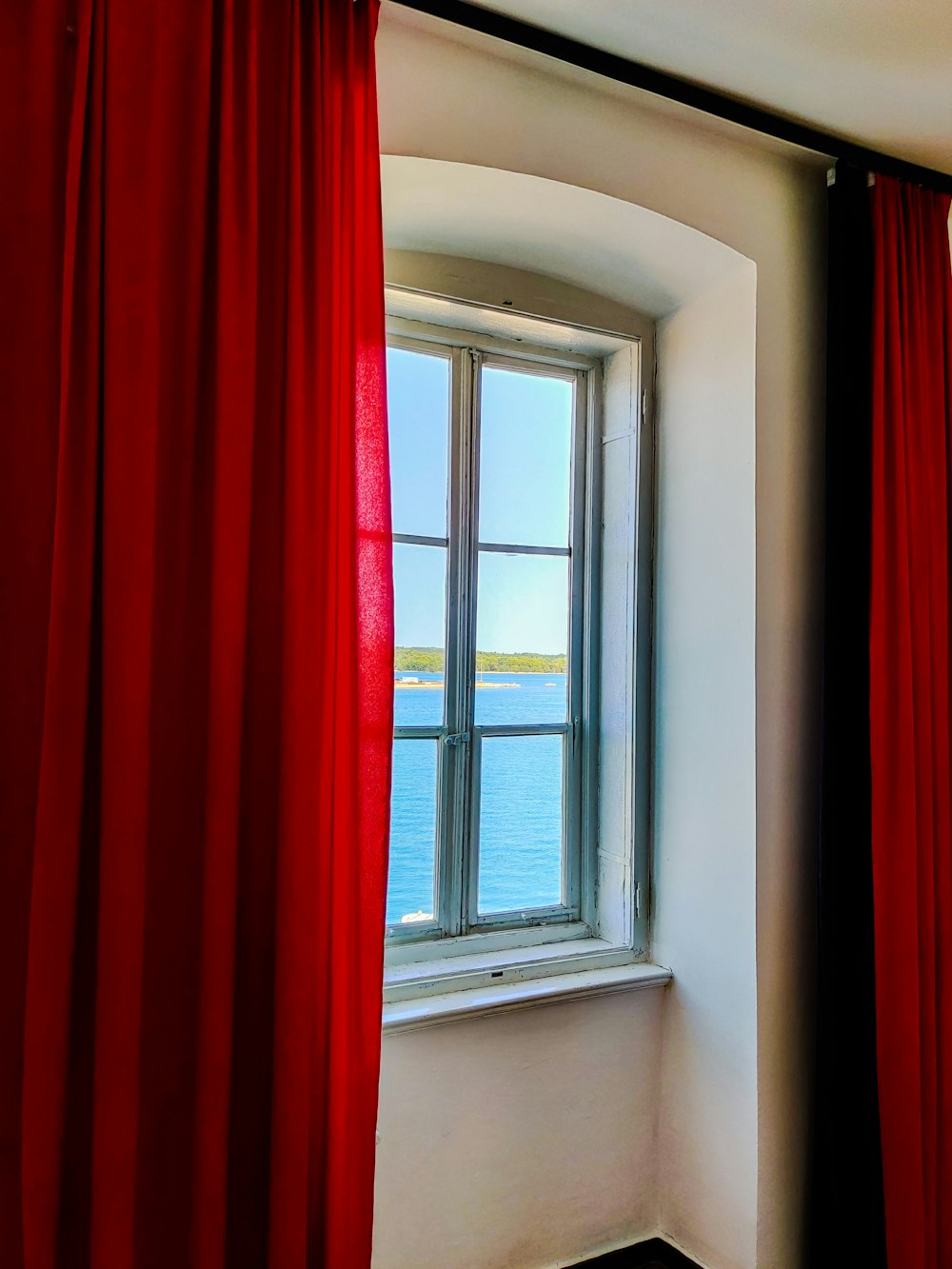 a window with a red curtain and a view of the ocean