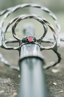 A close-up view of a sword hilt with intricate metalwork and a prominent red gemstone set in the center. The focus is on the handle, with the blade extending into a blurred background, emphasizing the details of the craftsmanship.