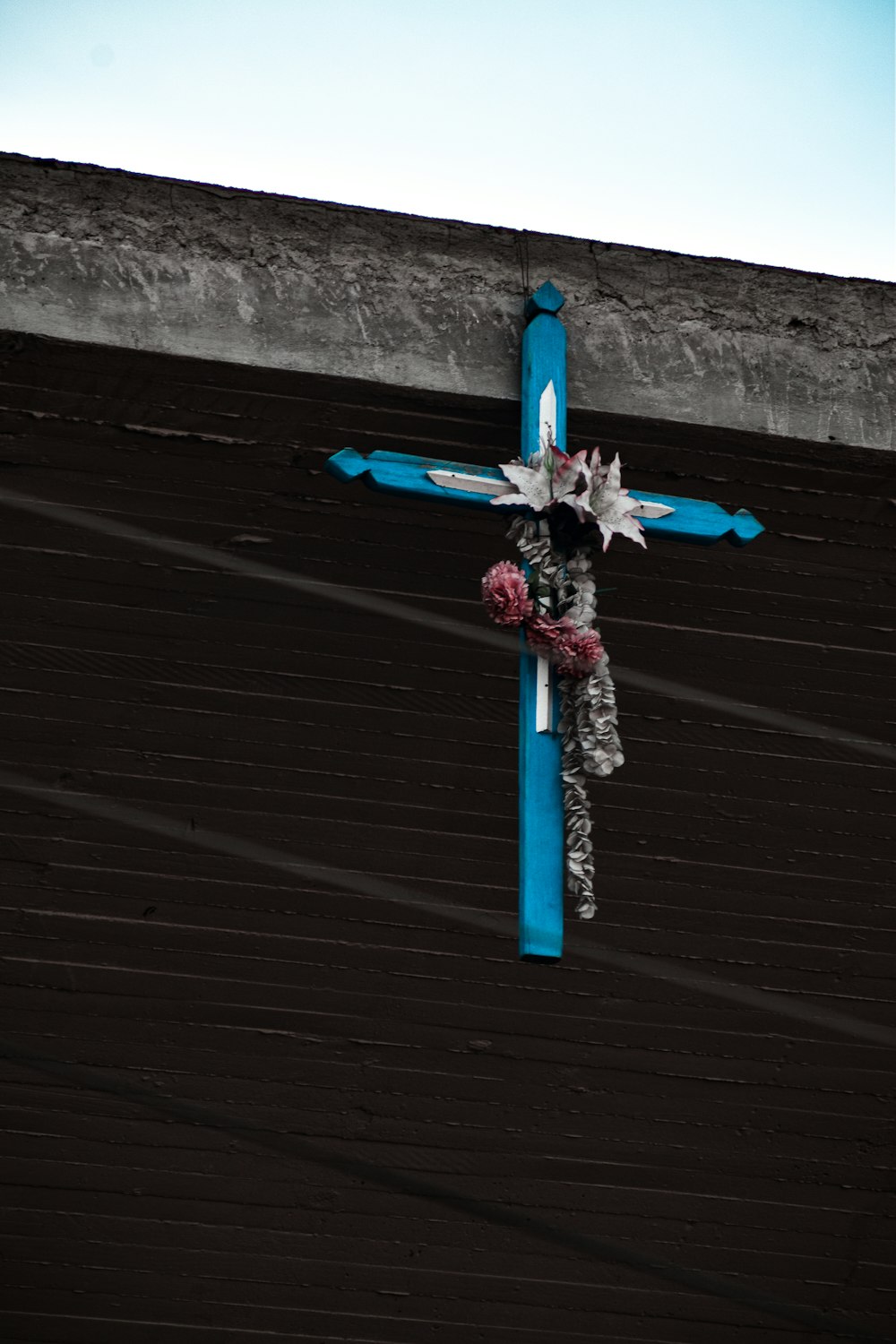 a blue cross with flowers on it on the side of a building