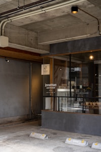 A modern storefront with concrete walls and exposed industrial pipes is visible. The store has a large window display with some products inside, including a sign labeled 'jonathan supermarket'. The lighting is subtle, with a warm-colored spotlight illuminating part of the ceiling.