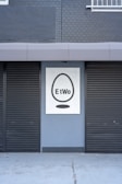 A building facade featuring two closed black shutters and a sign with a black egg shape and the word 'EtWo' on a grey brick wall.