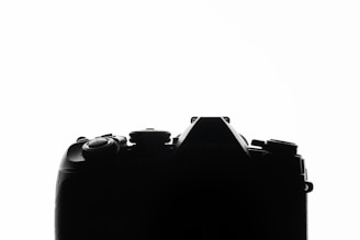 The image features a silhouette of a camera against a white background, highlighting the camera's shape and intricate details of the buttons and dials.