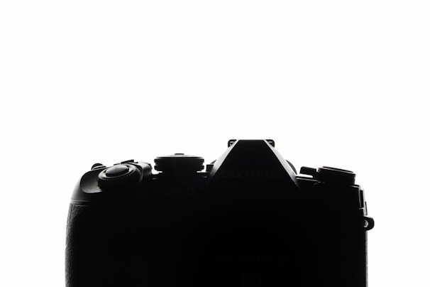 The image features a silhouette of a camera against a white background, highlighting the camera's shape and intricate details of the buttons and dials.