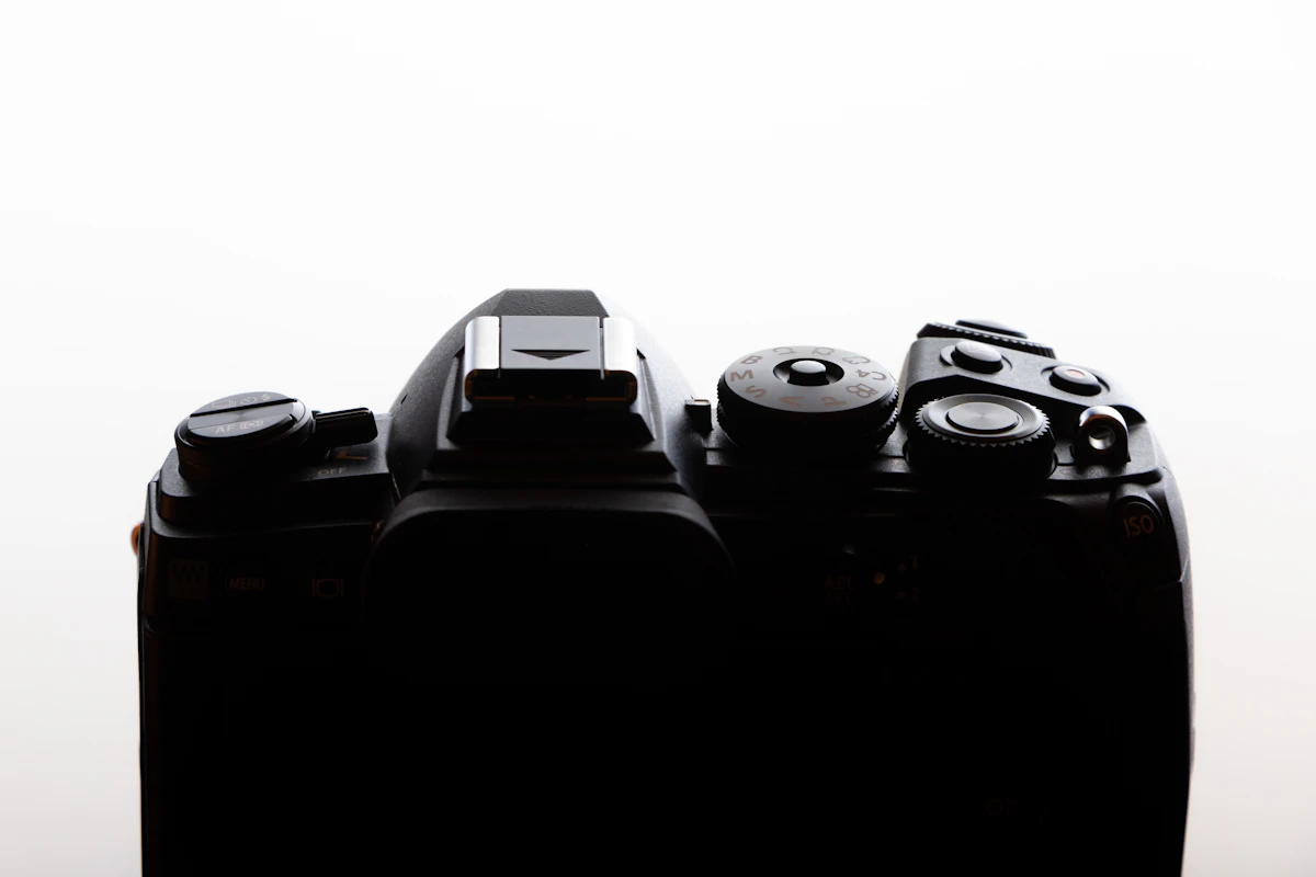 Macro of a camera's top-plate mode dial, shutter button, and hot shoe against a white background.