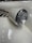 Close-up of a vintage car's front headlight with a white and chrome finish. The car's elegant, curved design is accentuated by smooth lines and a polished surface, highlighting its classic style. Part of the car's emblem and side exhaust pipes are visible, adding to the retro aesthetic.