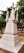 An ornately carved stone monument with a cross on top, surrounded by greenery in a cemetery setting. The monument features detailed architectural elements and a weathered appearance.