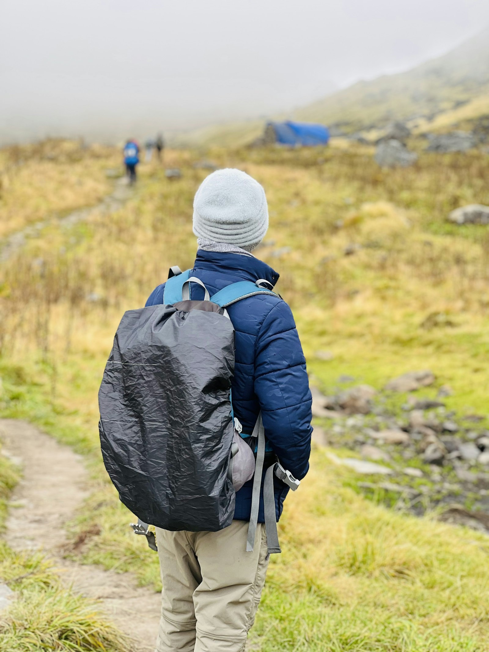 Un randonneur de dos, son sac recouvert d’une housse grise