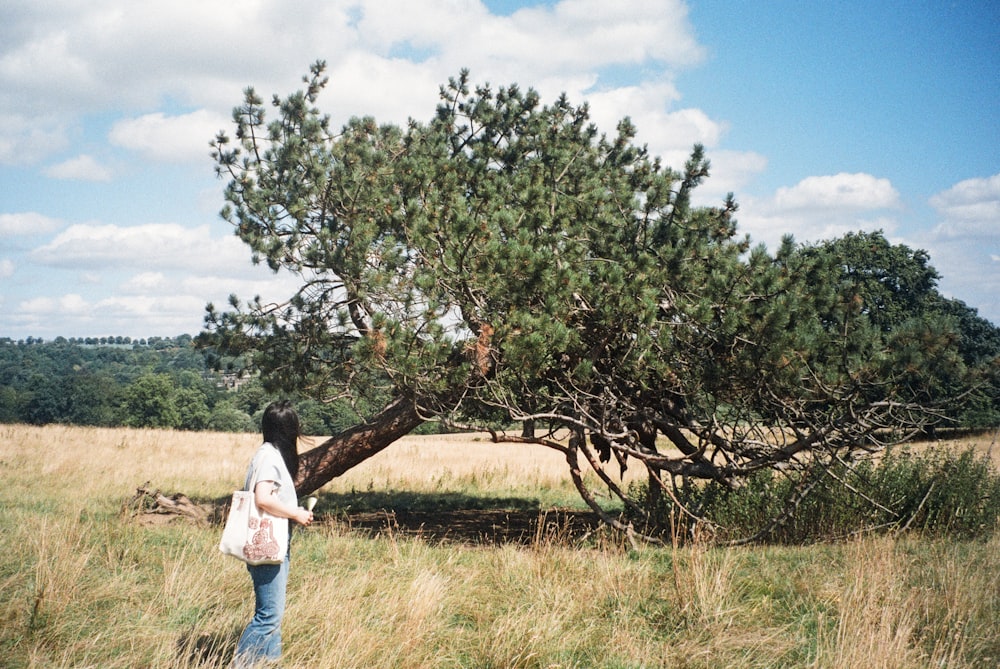 a woman standing in a field next to a tree