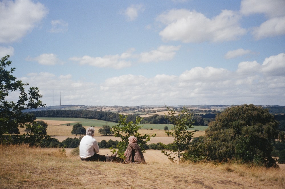 a couple of people sitting on top of a grass covered hillside