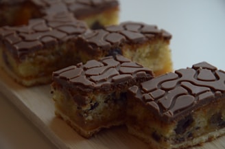 Several pieces of cake with a patterned chocolate topping on a wooden surface. The cake has a light, fluffy texture with visible chocolate chips and a rich brown chocolate top with intricate swirls.