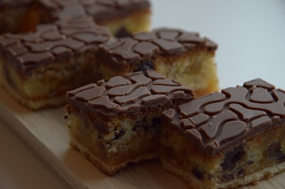 Several pieces of cake with a patterned chocolate topping on a wooden surface. The cake has a light, fluffy texture with visible chocolate chips and a rich brown chocolate top with intricate swirls.