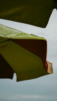 Close-up view of green and orange outdoor umbrellas positioned against a cloudy sky backdrop.