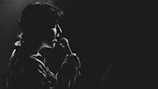 A person is singing into a microphone, captured in silhouette against a dark background. The lighting creates a dramatic effect, highlighting the contours of their face and the microphone.