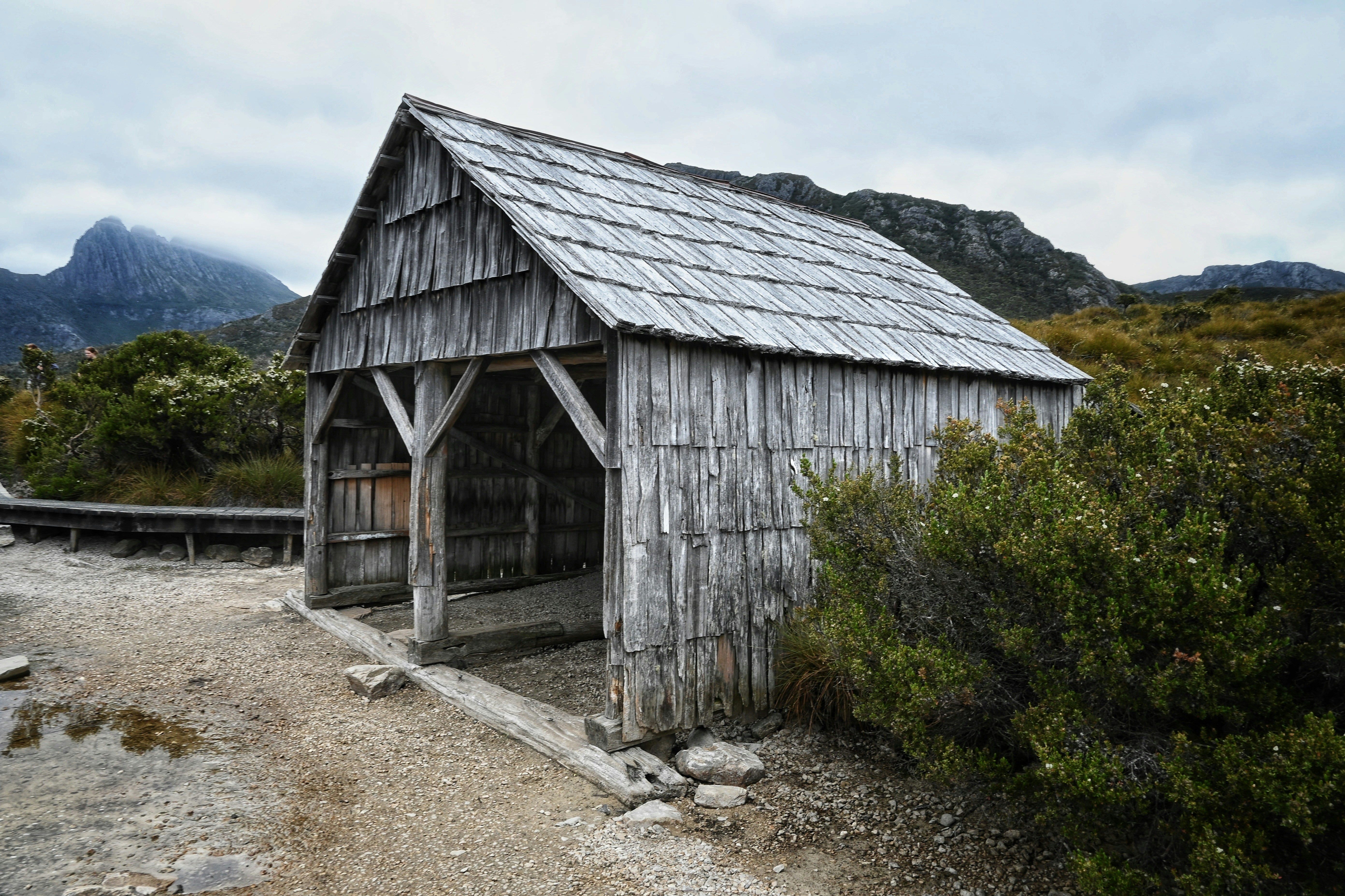 a small wooden building sitting on top of a dirt road, A westerly view of Dove Lake Boatshed along the Dove Lake Circuit, Cradle Mtn-Lake St Clair National Park, Tasmania.