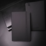 Custom branded notebooks with charcoal covers and embossed logos arranged neatly on a white surface.