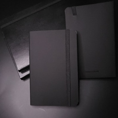Custom branded notebooks with charcoal covers and embossed logos arranged neatly on a white surface.