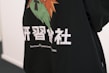 A close-up of a garment, such as a shirt or hoodie, adorned with a colorful graphic consisting of orange, green, and black colors. Below the graphic, there is text in white, which includes both large Chinese characters and smaller English text that reads 'TeenTeam Canton Local'.