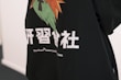 A close-up of a garment, such as a shirt or hoodie, adorned with a colorful graphic consisting of orange, green, and black colors. Below the graphic, there is text in white, which includes both large Chinese characters and smaller English text that reads 'TeenTeam Canton Local'.