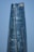 A modern skyscraper with a sleek, curved design and reflective glass facade that mirrors the clear blue sky. The building features a golden crown logo near the top.