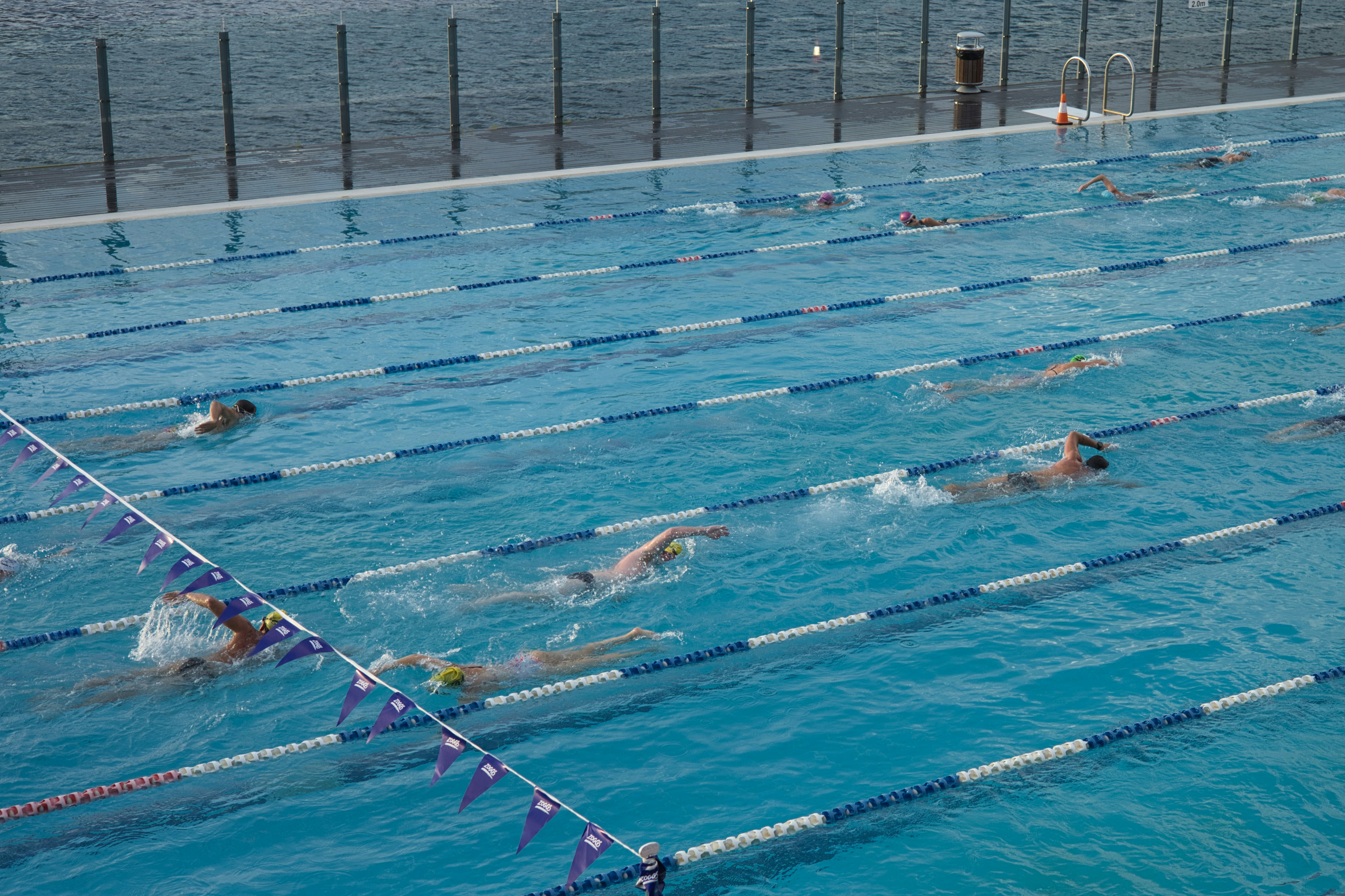 Swimmer diving into an outdoor pool with clear blue water, bright sunny day, competitive swimming setting