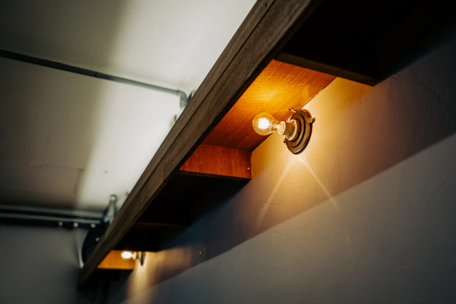 Close-up of a floating walnut shelf with soft amber LED lighting highlighting the wood grain against a dark modern wall.