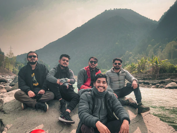 Travelers enjoying a peaceful moment sitting on rocks near a flowing river in the forest.