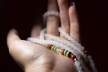 Hand holding a string of red, black, and white beads with a blurred altar background.