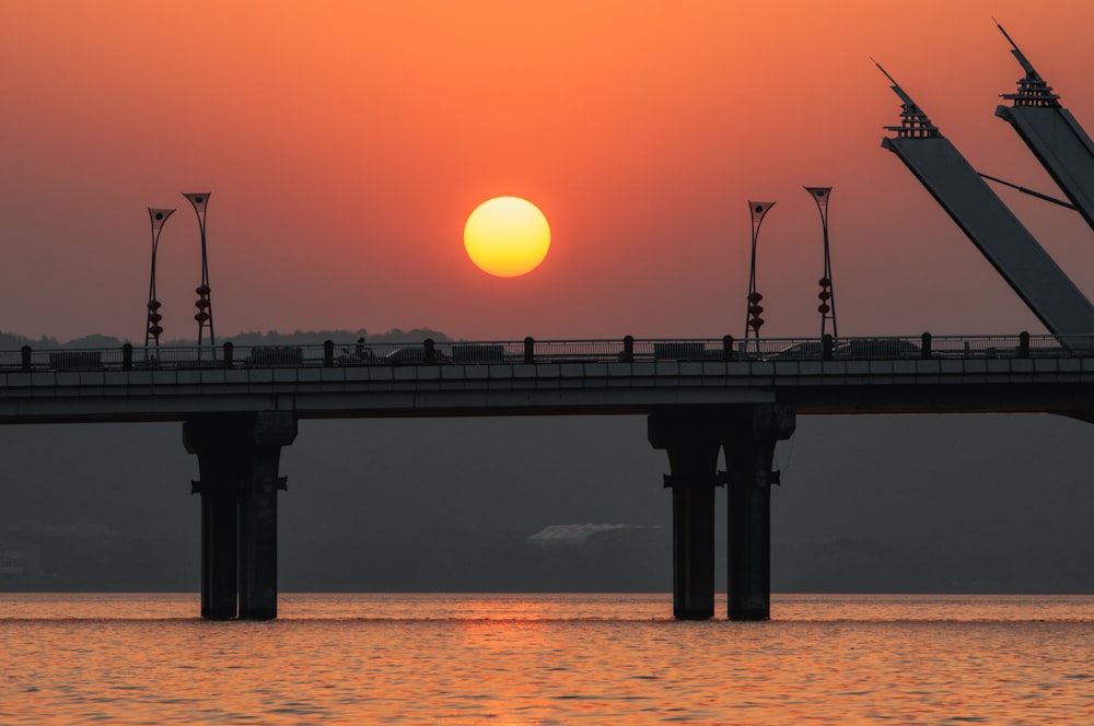 the sun is setting over a bridge over a body of water