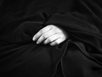 Minimalist composition showing elegant fabric folds and a discreet hand gesture in black and white.