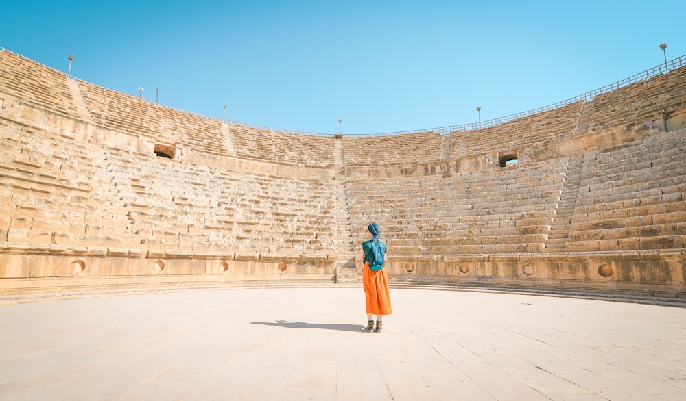 a woman standing in an empty arena in front of a stone wall