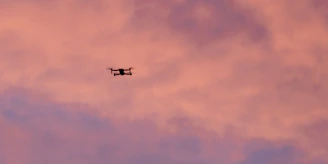A sleek drone soaring against a clear blue sky at sunset.