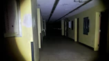 A dimly lit office corridor rapidly filling with dense yellowish fog from a wall-mounted shockfog device.