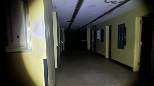 A dimly lit office corridor rapidly filling with dense yellowish fog from a wall-mounted shockfog device.