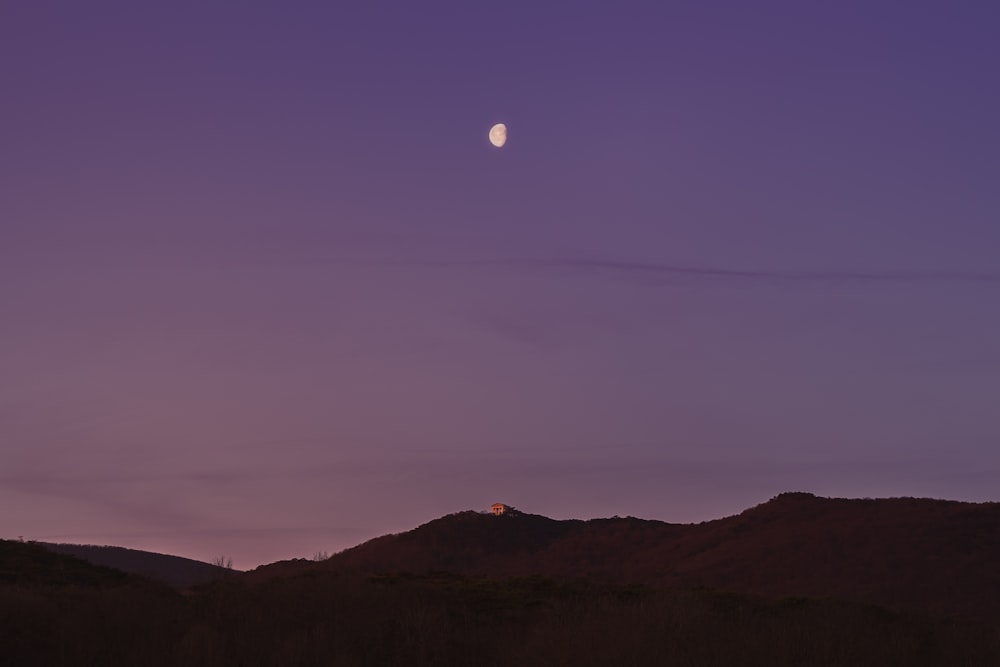 the moon is setting over a mountain range