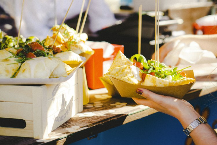 Colorful food stalls lined up at an outdoor festival with visitors browsing the offerings
