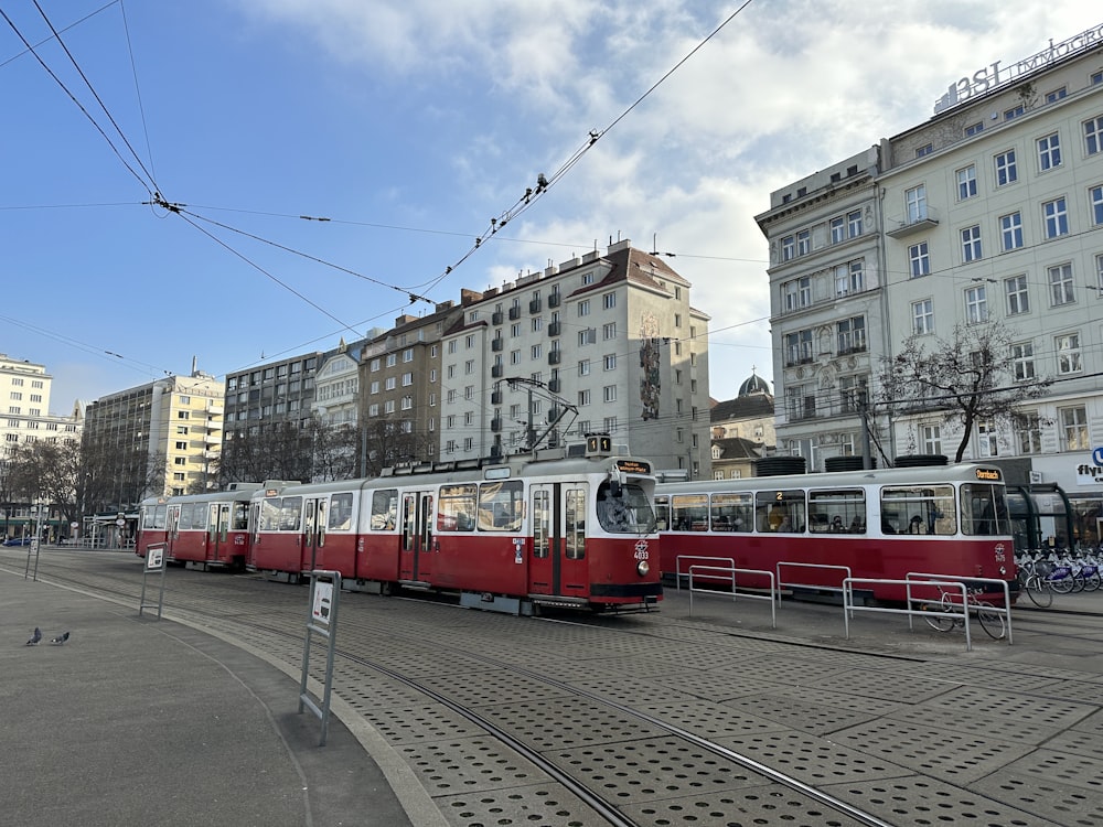 a red and white train traveling down a street next to tall buildings