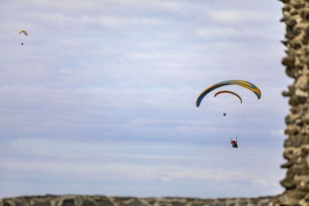 two parasailers are flying over a rocky cliff